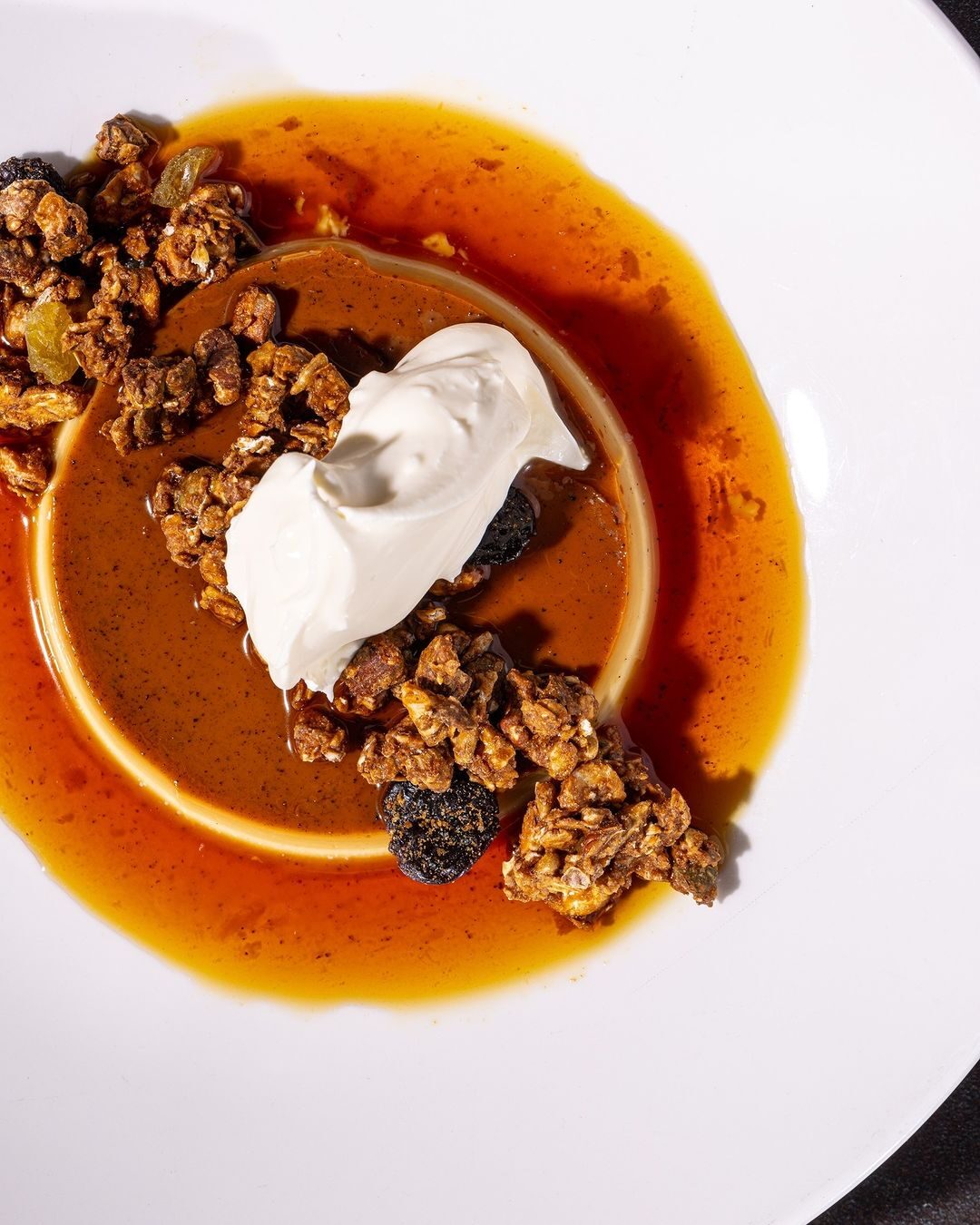 Caramel dessert with granola and cream on a white plate